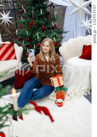 Happy blonde woman taking selfie with Christmas gift by festive tree Happy blonde woman taking selfie with Christmas gift by festive tree 132353547