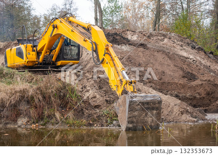 Excavator digging artificial water basin. Long arm of an excavator spreading banks of a pond, making it bigger Excavator digging artificial water basin. Long arm of an excavator spreading banks of a pond, making it bigger 132353673