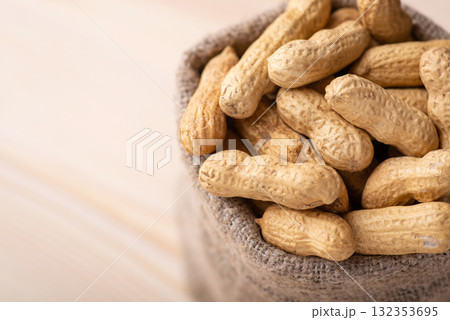 Bag with peanuts on wooden background. Close up of unpeeled peanuts, harvest of nuts 132353695