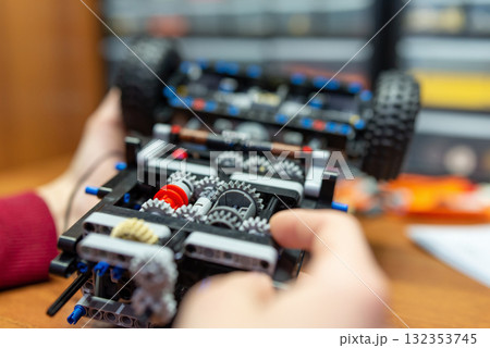 Complex mechanism of a toy car made by a boy in his hands. Little boy playing with engineering set for making different machines Complex mechanism of a toy car made by a boy in his hands. Little boy playing with engineering set for making different machines 132353745