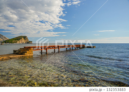 Panoramic view of the Adriatic Sea with an old rusty pier in Budva, Montenegro. Atmospheric coastal landscape with calm waters and seaside scenery. 132353883