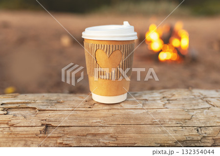 Paper cup of natural coffee with carved heart on log against background of fire beach in European city Paper cup of natural coffee with carved heart on log against background of fire beach in European city 132354044