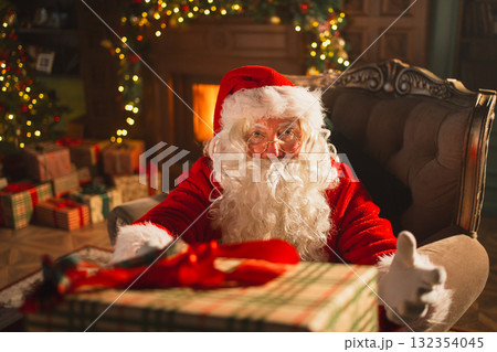 Merry Christmas. Santa Claus giving you present gift box in festive living room with fireplace decorations Christmas tree. Santa packing wrapping gift box on Christmas eve. Winter Holiday Celebrations 132354045