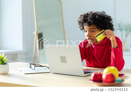 African american woman using laptop shopping online paying with gold credit card. Girl sitting at home buying on Internet enter credit card details. Online shopping ecommerce delivery service African american woman using laptop shopping online paying with gold credit card. Girl sitting at home buying on Internet enter credit card details. Online shopping ecommerce delivery service 132354113