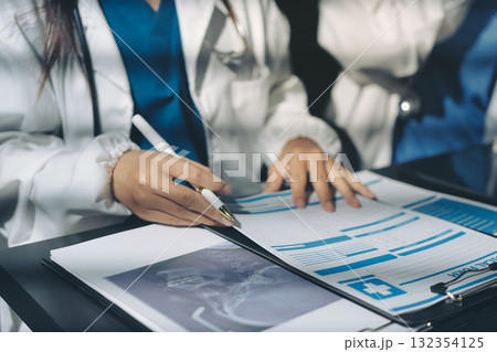 Two doctors and a female nurse meet at a table in the hospital, collaborating on medical tasks using laptops and computers Two doctors and a female nurse meet at a table in the hospital, collaborating on medical tasks using laptops and computers 132354125