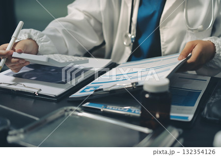 Two doctors and a female nurse meet at a table in the hospital, collaborating on medical tasks using laptops and computers Two doctors and a female nurse meet at a table in the hospital, collaborating on medical tasks using laptops and computers 132354126
