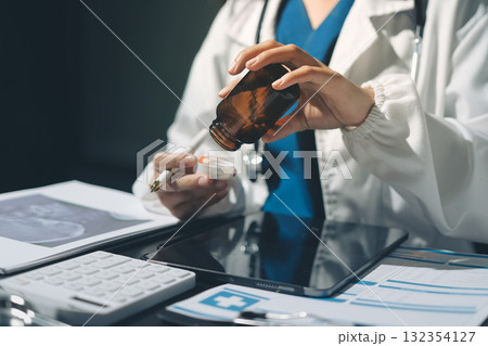 Two doctors and a female nurse meet at a table in the hospital, collaborating on medical tasks using laptops and computers 132354127