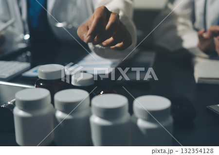 Two doctors and a female nurse meet at a table in the hospital, collaborating on medical tasks using laptops and computers Two doctors and a female nurse meet at a table in the hospital, collaborating on medical tasks using laptops and computers 132354128