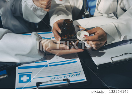 Two doctors and a female nurse meet at a table in the hospital, collaborating on medical tasks using laptops and computers 132354143