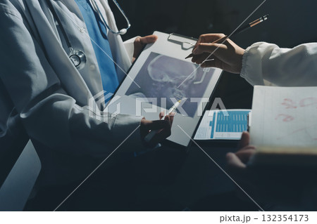 Two doctors and a female nurse meet at a table in the hospital, collaborating on medical tasks using laptops and computers 132354173