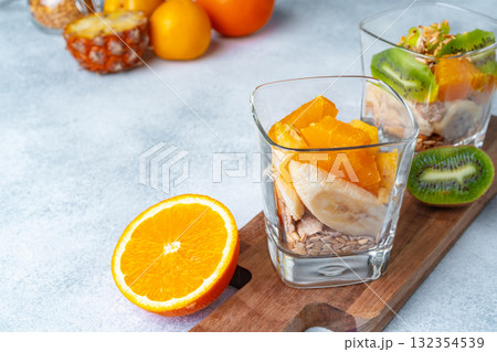 Glass with fruit pieces and oatmeal muesli on wooden board 132354539