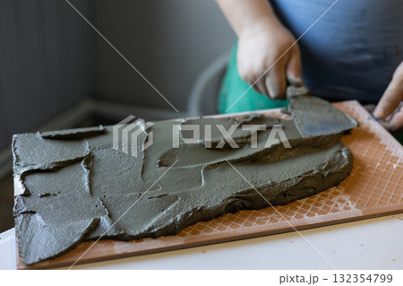 A person carefully applies tile adhesive to the back of a ceramic tile using a trowel. Preparing tiles for installation during a home renovation or DIY project. Laying tiles on a wall. 132354799