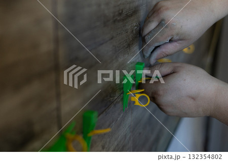 Laying wall tiles. The dirty hands of a worker laying new ceramic tiles on a wall using a leveling system symbolizes home renovation, floor repair, and construction work. 132354802
