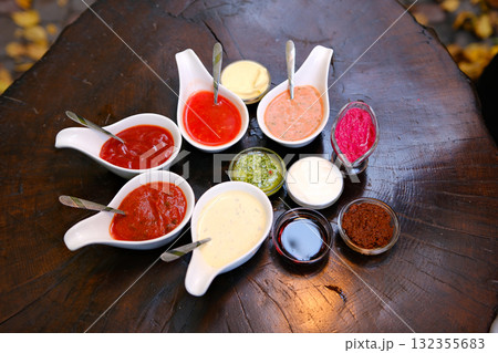 Various types of sauces are neatly arranged in small glass jars, showcasing vibrant colors and textures. The selection includes red, green, and brown sauces against a clean surface. 132355683