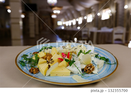 Cheese, bread, red wine, and walnuts on a kitchen table. In the background various wine bottles. Selective focus. Cheese, bread, red wine, and walnuts on a kitchen table. In the background various wine bottles. Selective focus. 132355700