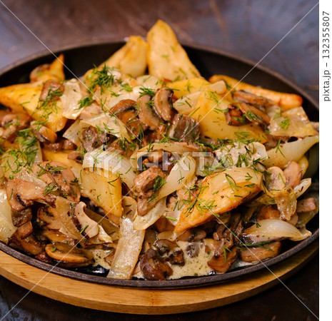 Boiled and fried baby potatoes in peels with fried champignon mushrooms and spices a black frying pan. Green background, top view 132355807