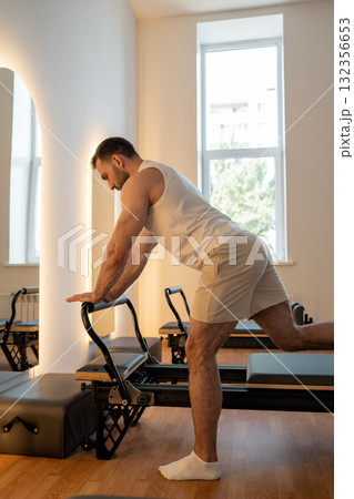 Man training pilates on the reformer bed. Reformer pilates studio machine for fitness workouts in gym. Fit, healthy and strong authentical body. Fitness concept Man training pilates on the reformer bed. Reformer pilates studio machine for fitness workouts in gym. Fit, healthy and strong authentical body. Fitness concept 132356653