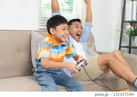 Family Bonding and Gaming. A father and son joyfully playing video games together on a cozy couch. 132357149