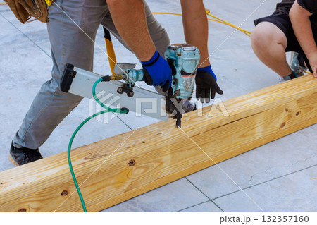 Two workers on securing wooden beams with air nail gun at construction site Two workers on securing wooden beams with air nail gun at construction site 132357160