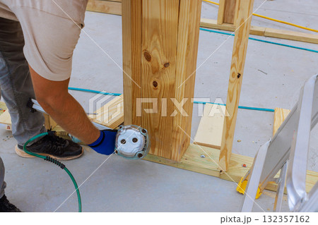 Contractor operates air nail gun on wooden post at busy construction site, building work. Contractor operates air nail gun on wooden post at busy construction site, building work. 132357162