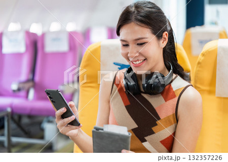Tourist and Air Travel Experience. A young woman enjoying her flight while using her smartphone and headphones. 132357226