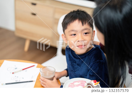 Snack Time and Learning. A young boy enjoying a snack while engaging in a conversation with a family member. Snack Time and Learning. A young boy enjoying a snack while engaging in a conversation with a family member. 132357570