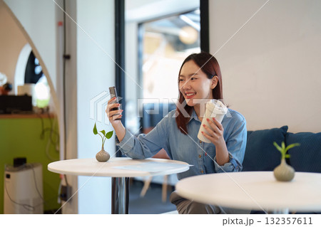Leisure and Relaxation. A young customer enjoys her coffee while using her phone in a cozy cafe setting. 132357611