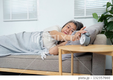 Morning Routine and Wellness. An elderly woman waking up peacefully and reaching for her alarm, embodying a positive start to the day. 132357660