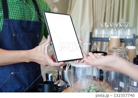Sustainability and Customer Interaction. A barista presents a menu on a tablet, showcasing tech in promoting eco-conscious coffee options. 132357740