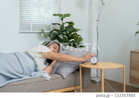 Morning Awakening and Self-Care. An elderly woman waking up and turning off her alarm, symbolizing a refreshing start to the day. Morning Awakening and Self-Care. An elderly woman waking up and turning off her alarm, symbolizing a refreshing start to the day. 132357805