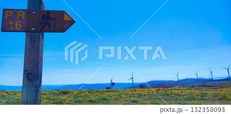 Hiking trail marker on a hill in northern Portugal. Wildflowers with wind turbines - ecotourism, renewable energy and nature adventure trail in Portugal Hiking trail marker on a hill in northern Portugal. Wildflowers with wind turbines - ecotourism, renewable energy and nature adventure trail in Portugal 132358093