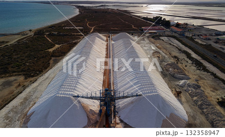 Aerial view of large salt piles and industrial conveyor system near the coast of Santa Pola, Spain, with salt ponds and the sea in the background. 132358947
