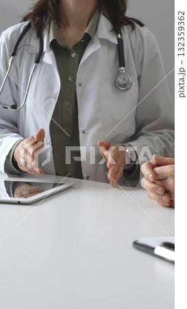 Doctor woman in medical coat is explaining diagnosis to patient man during a medical consultation in clinic office, gesturing with hands over a desk, vertical close up view. Medicine and health care Doctor woman in medical coat is explaining diagnosis to patient man during a medical consultation in clinic office, gesturing with hands over a desk, vertical close up view. Medicine and health care 132359362