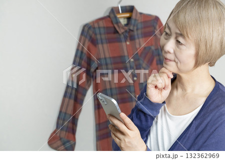 不要になった洋服をフリマサイトに出品するためにスマホで撮影するシニア女性 132362969