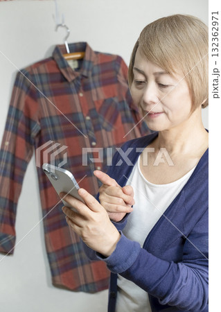 不要になった洋服をフリマサイトに出品するためにスマホで撮影するシニア女性 不要になった洋服をフリマサイトに出品するためにスマホで撮影するシニア女性 132362971