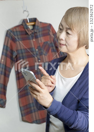 不要になった洋服をフリマサイトに出品するためにスマホで撮影するシニア女性 132362972