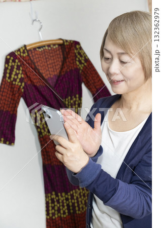 不要になった洋服をフリマサイトに出品するためにスマホで撮影するシニア女性 132362979