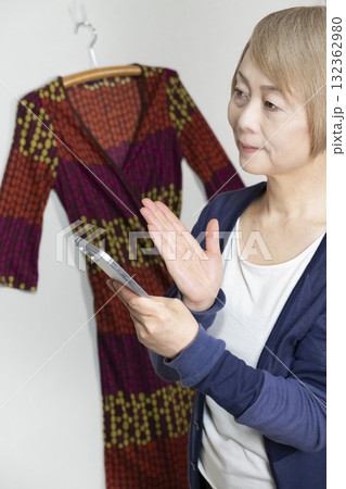 不要になった洋服をフリマサイトに出品するためにスマホで撮影するシニア女性 132362980