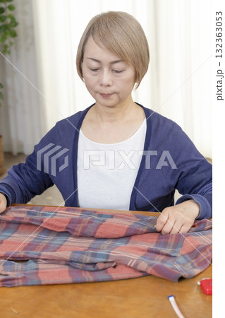 リビングで不要になった洋服をフリマサイトに出品するために洋服を梱包するシニア女性 リビングで不要になった洋服をフリマサイトに出品するために洋服を梱包するシニア女性 132363053