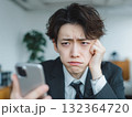 困った表情のビジネスマン、スマホを見て悩む様子を表現 132364720