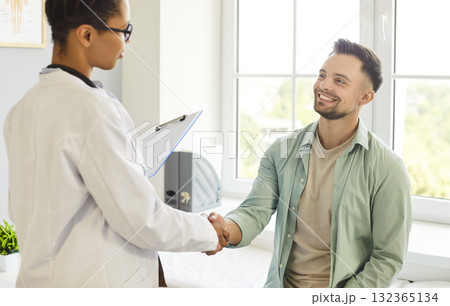 Friendly doctor shaking hands with a young patient standing in medical clinic Friendly doctor shaking hands with a young patient standing in medical clinic 132365134