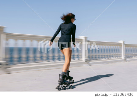 Woman rollerblading along seaside promenade in black outfit, active lifestyle and freedom concept 132365436