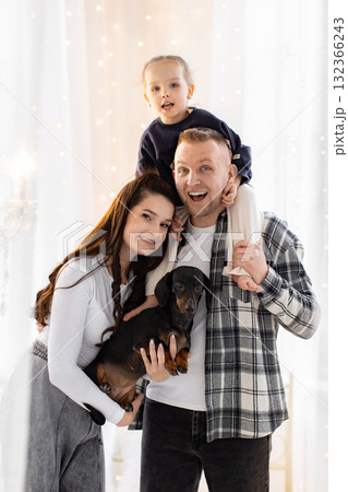 A happy family poses together, featuring a father, mother, daughter, and their adorable dachshund dog, creating a heartwarming scene. A happy family poses together, featuring a father, mother, daughter, and their adorable dachshund dog, creating a heartwarming scene. 132366243