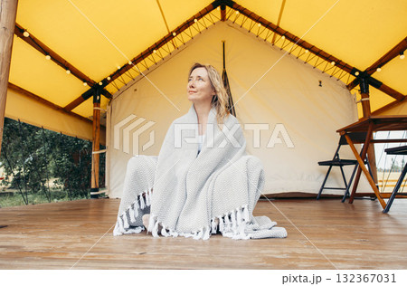 woman wrapped in cozy blanket on wooden terrace of glamping tent in morning light, barefoot and thoughtful, outdoor retreat, rustic furniture, countryside tranquility, slow living woman wrapped in cozy blanket on wooden terrace of glamping tent in morning light, barefoot and thoughtful, outdoor retreat, rustic furniture, countryside tranquility, slow living 132367031