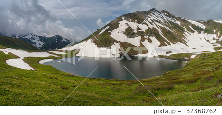 Mountain peaks, green grass and cold lake in the foreground. Mountain peaks, green grass and cold lake in the foreground. 132368762