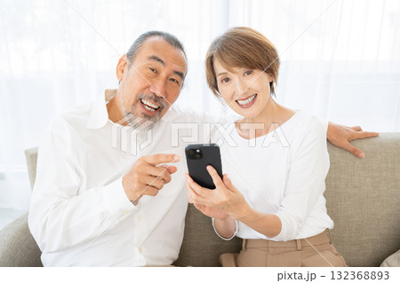 ソファでくつろぎながらスマホを操作するシニア夫婦 132368893