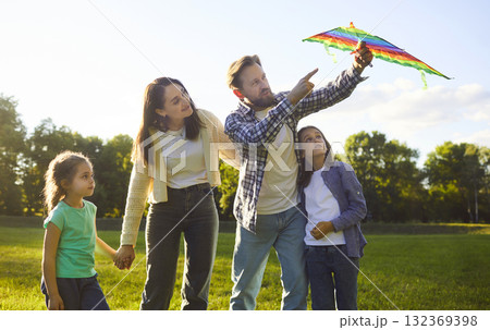 Happy cheerful family of four standing in summer park at sunset playing with flying kite in nature 132369398