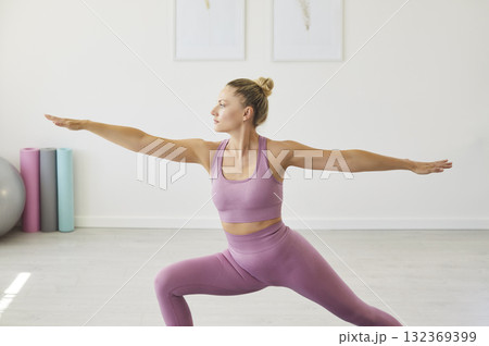 Young woman practicing yoga warrior pose in a bright home fitness studio Young woman practicing yoga warrior pose in a bright home fitness studio 132369399
