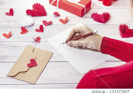 girl writes a love letter against the background of a gift and red hearts girl writes a love letter against the background of a gift and red hearts 132372607
