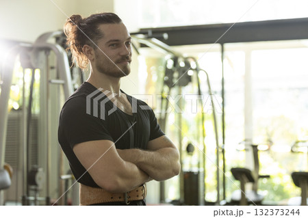 Confident muscular man standing with arms crossed in modern gym, showcasing strength, fitness dedication, and healthy lifestyle motivation in a workout environment. Confident muscular man standing with arms crossed in modern gym, showcasing strength, fitness dedication, and healthy lifestyle motivation in a workout environment. 132373244